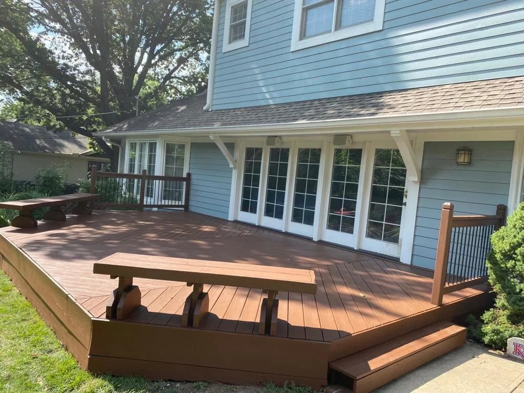 Brown stained deck with built-in benches and black railings beside a blue house